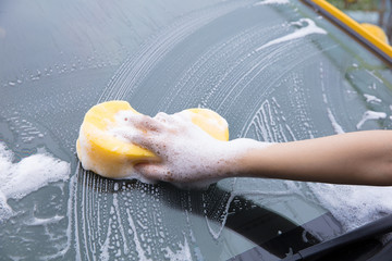 cleaning windscreen of a car with yellow sponge foam.