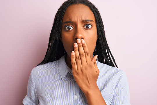 Young african american woman wearing striped shirt standing over isolated pink background cover mouth with hand shocked with shame for mistake, expression of fear, scared in silence, secret concept