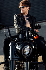 Fototapeta na wymiar shirtless handsome young man in leather jacket resting on black motorcycle