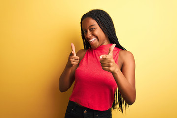 African american woman wearing red casual t-shirt standing over isolated yellow background pointing fingers to camera with happy and funny face. Good energy and vibes.