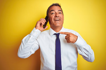 Middle age businessman talking on the smartphone over isolated yellow background very happy pointing with hand and finger