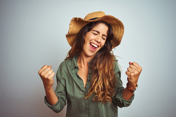 Young beautiful woman on vacation wearing green shirt and hat over white isolated background very happy and excited doing winner gesture with arms raised, smiling and screaming for success. 