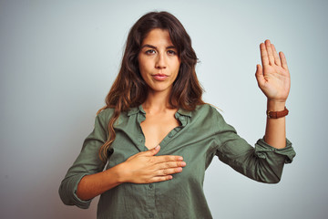 Young beautiful woman wearing green shirt standing over grey isolated background Swearing with hand...