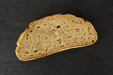 One slice of fresh baked rye wheat bread flatlay on grey stone