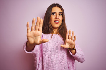 Young beautiful woman wearing casual sweater standing over isolated pink background afraid and terrified with fear expression stop gesture with hands, shouting in shock. Panic concept.