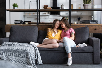 two smiling lesbians holding hands while sitting on sofa in living room