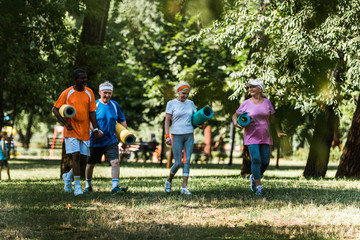 Fototapeta premium selective focus of happy senior and multicultural pensioners holding fitness mats and walking on grass