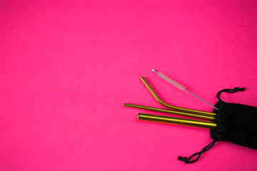 reusable stainless steel straws and cleaning brush in black velvet bag on pink background, eco friendly lifestyle