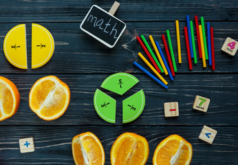 Сolorful math fractions and oranges as a sample on dark wooden background or table. Interesting...