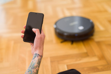 Close up of man hands controling automatic vacuum cleaner using electronic control of the mopping...