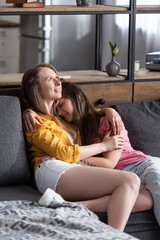 two pretty lesbians embracing while sitting on sofa in living room
