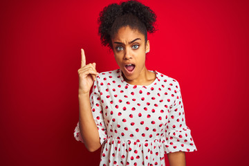 African american woman wearing fashion white dress standing over isolated red background pointing finger up with successful idea. Exited and happy. Number one.