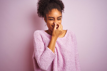 Young african american woman wearing winter sweater standing over isolated pink background smelling...