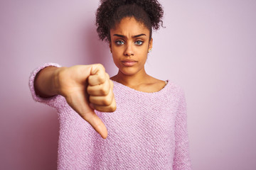 Young african american woman wearing winter sweater standing over isolated pink background looking unhappy and angry showing rejection and negative with thumbs down gesture. Bad expression.