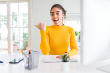 Young african american girl working using computer pointing and showing with thumb up to the side with happy face smiling