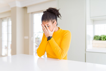 Beautiful african american woman with afro hair wearing a casual yellow sweater with sad expression covering face with hands while crying. Depression concept.