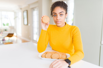 Young african american girl eating healthy whole grain biscuits with a confident expression on smart face thinking serious