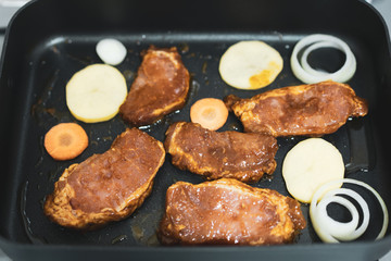 Roasting pork steak on a black pan with some of sliced vegetable; carrot, onion and potapo.  Home made steak with sweet and spicy sauce.
