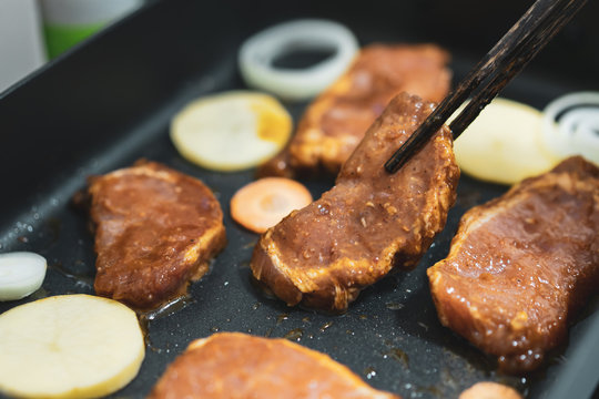 Roasting pork steak on a black pan with some of sliced vegetable; carrot, onion and potapo.  Home made steak with sweet and spicy sauce.