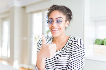 Beautiful young african american woman with afro hair wearing glasses doing happy thumbs up gesture with hand. Approving expression looking at the camera showing success.