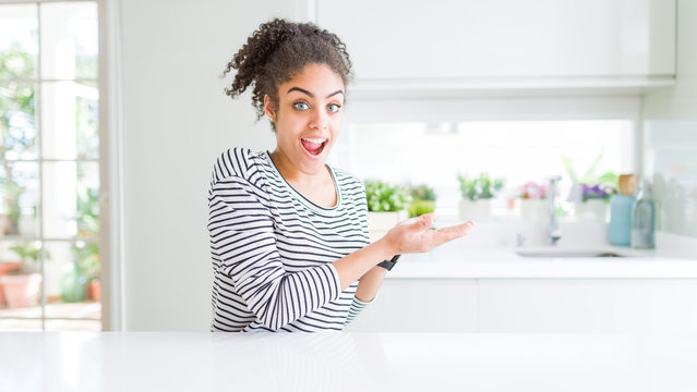 Beautiful african american woman with afro hair wearing casual striped sweater pointing aside with hands open palms showing copy space, presenting advertisement smiling excited happy