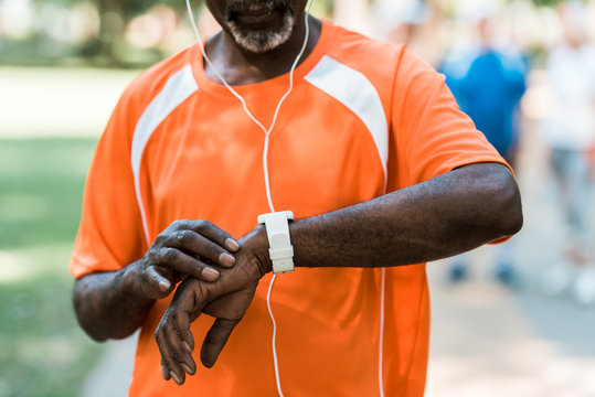 cropped view of senior african american man in earphones touching smart watch