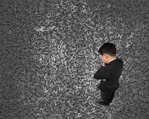 Big data concept, Thinking business man standing and looking at huge amount of 3d dark grey concrete letters and numbers texture background.