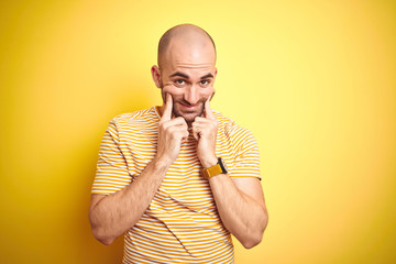 Young bald man with beard wearing casual striped t-shirt over yellow isolated background Smiling with open mouth, fingers pointing and forcing cheerful smile