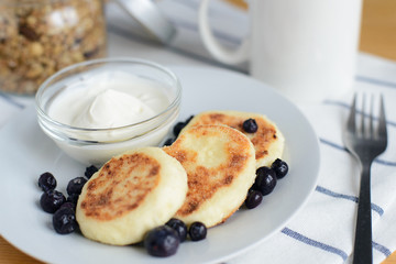 eastern european breakfast, fried circular syrniki, tvorozhniki or cheese cake with sour cream and hot drink on wooden table, close up view from above of horizontal still life stock photo image