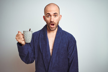 Young man wearing a bathrobe drinking a cup of coffee in the morning over isolated background scared in shock with a surprise face, afraid and excited with fear expression