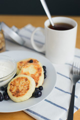 eastern european breakfast, fried circular syrniki, tvorozhniki or cheese cake with sour cream and hot drink on wooden table, close up view from above of vertical still life stock photo image