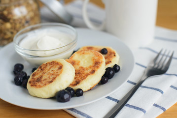 eastern european breakfast, fried circular syrniki, tvorozhniki or cheese cake with sour cream and hot drink on wooden table, close up view from above of horizontal still life stock photo image