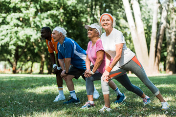 Naklejka premium selective focus of happy senior and multicultural people doing stretching exercise on grass