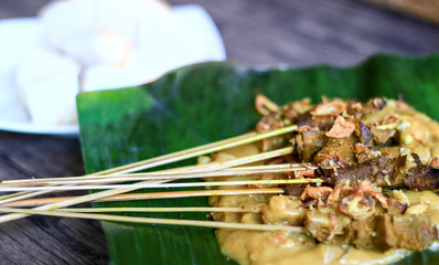 Sate Padang or Padang Satay and ketupat (traditional rice cake) on banana leaf.  Wood background.