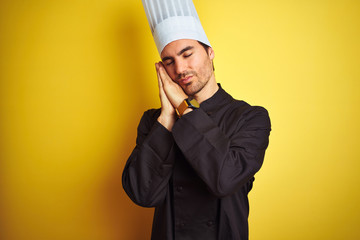 Young chef man wearing uniform and hat standing over isolated yellow background sleeping tired dreaming and posing with hands together while smiling with closed eyes.