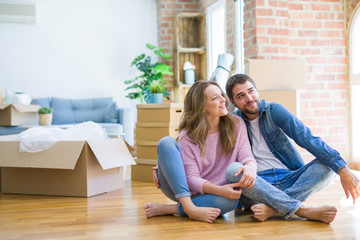 Young beautiful couple moving to a new house sitting on the floor looking away to side with smile on face, natural expression. Laughing confident.