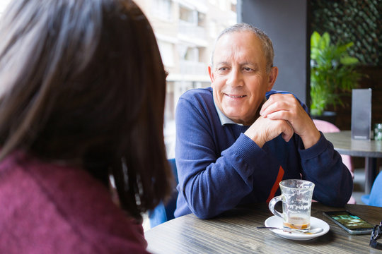 Senior man having a conversation with woman drinking coffee and relaxing, chatting at restaurant