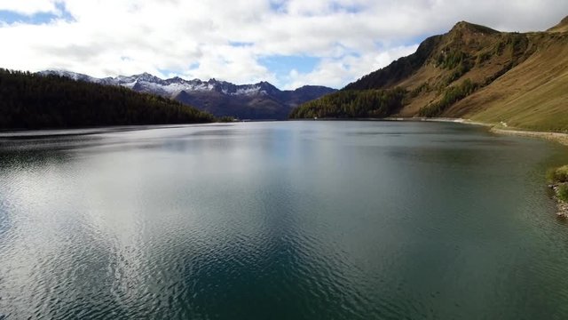 aerial view of mountain lake in Switzerland during autumn with colored pine tree forest, cloudy fall day with snowy mountains, lago ritom