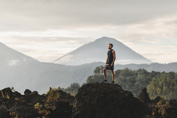 Young man standing on top of stone and enjoying amazing volcanic mountain Agung view in Bali. Travel and active lifestyle concept.
