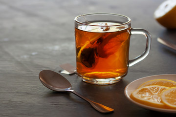 Cup of tea with tea bag and lemon slices on dark background