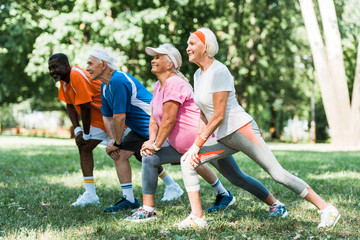selective focus of happy retired and multicultural people doing stretching exercise on grass