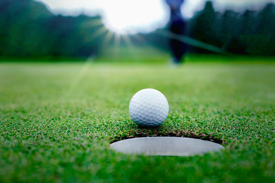 Golf balls and golf club on green grass shiny light sunse