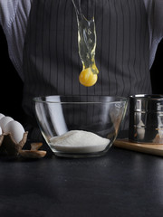 man break egg in bowl. recipe of pie making on dark background