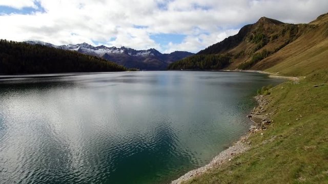 aerial view of mountain lake in Switzerland during autumn with colored pine tree forest, cloudy fall day with snowy mountains, lago ritom