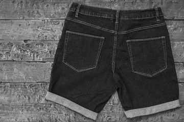 Black and white image of denim shorts with cuffs on wooden background. Fashionable unisex clothing.