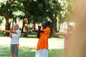 selective focus of happy milticultural retired women and man working out in park