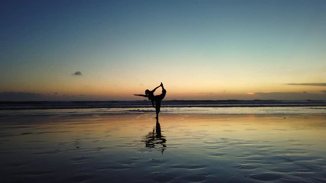Black girl with beautiful braids does yoga pose during sunset on a beach in Bali, Indonesia