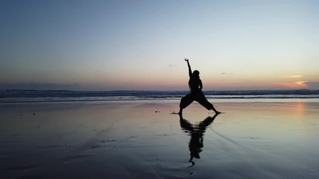 Black girl with beautiful braids does yoga pose during sunset on a beach in Bali, Indonesia