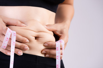 Fat woman hand holding excessive belly fat with measuring tape. Healthcare and woman diet lifestyle...