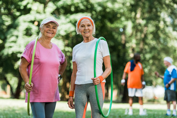 selective focus of sportive senior women smiling while holding hula hoops near multicultural...